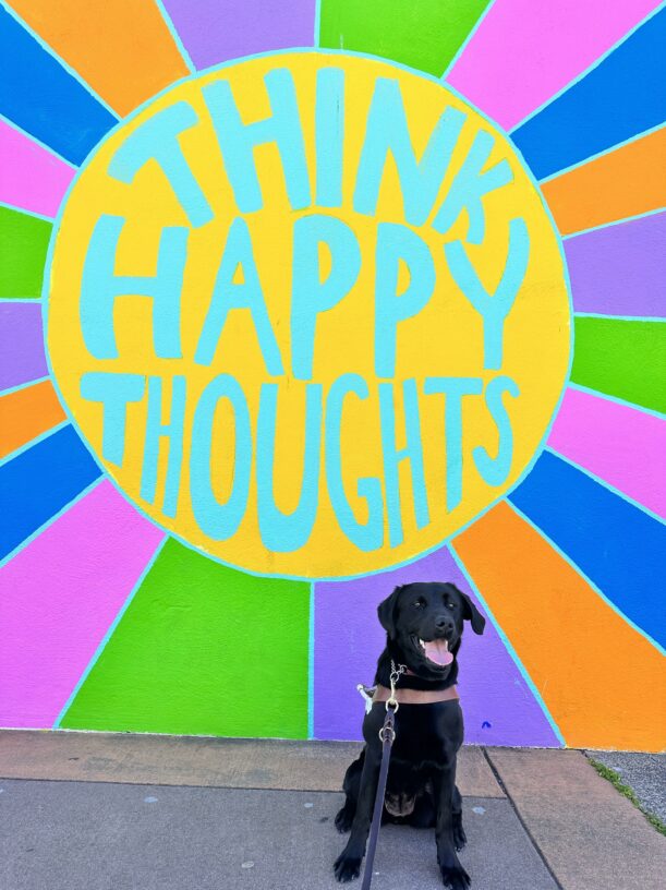 Natalia sitting in harness in front of a colorful sign that says 