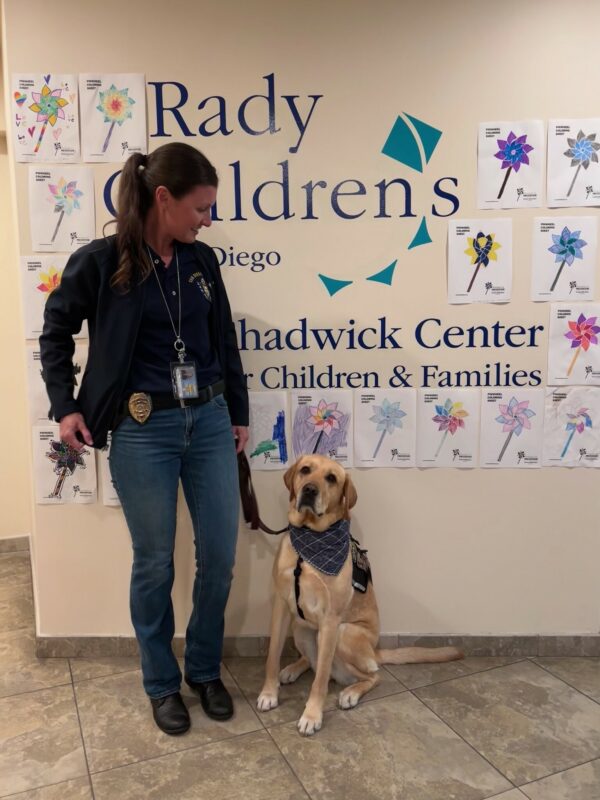 Lyle wears a vest and blue bandana and looks into the camera. He is accompanied by a police office as they visit a Children's center.