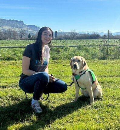 Raelyn poses with her apprentice trainer Phoebe on bright green grass. Raelyn is wearing a green vest.